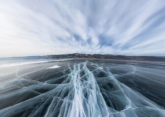 Wall Mural - Ice of Lake Baikal in cracks near the island at sunset under gray clouds. Wide panorama