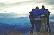 © Mint Images - Rear view of four people standing arm in arm on a mountain, snow-capped peaks in the distance.