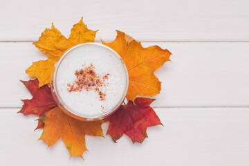 coffee latte with foam and cinnamon and yellow and red leaves on white table