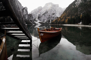 An old wooden boat stands near a boat station on a lake with a reflection of the mountains