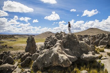 Poster - Beautiful view of a man standing on huge rock formations with a cloudy blue sky in the background