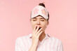 © Damir Khabirov - Close up portrait of teen girl in pyjama shirt and sleeping mask yawning and covering mouth, wanting to sleep, isolated on pink background