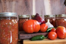 Fresh Tomatoes And Jalapenos From A Family Farm Vegetable Garden With Garlic And Red Onion For Home Canned Spicy Salsa In Glass Jars On A Rustic Background