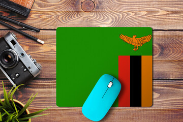 Wall Mural - Zambia flag on wooden background with blue wireless mouse on a mouse pad, top view. Digital media concept.