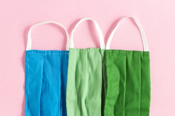 Poster - Closeup shot of blue, light green, and dark green protective face masks on a pink background