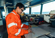 © Igor Kardasov - Filipino deck Officer on bridge of vessel or ship wearing coverall during navigaton watch at sea . He is plotting position on chart