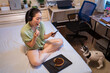 © Juan Alberto Ruiz - Young pretty Asian woman eating delicious chocolate tart on bed