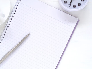 Blank notebook and pen with clock at 7:00 am, coffee cup on white work place desk table. Top view with space for text. Flat lay, Business and education concept..