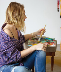 young beautiful woman artist drawing a picture with a palette of paints in hands