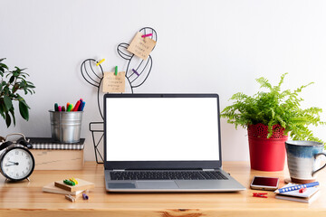 Laptop with blank screen on a table with coffee, phone and accessories and white empty wall with copy space. Work at home in office room with internet. Business and workpalce. Mock up.