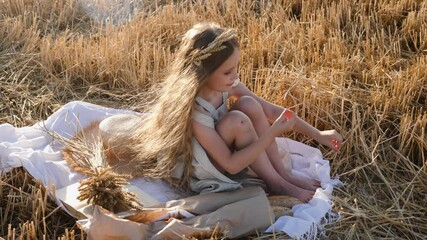 serious sad girl a child sit on a wheat mown field with a rim of ears on his head