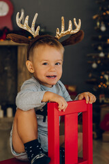 Baby boy with horns on his head on a red chair, on a background of a New Year decoration. Christmas and New Year. 