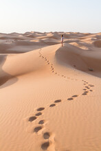 Blonde Female Caucasian Traveler Leaving Footprints In Sand Dunes When Walking In Dessert In Oman.