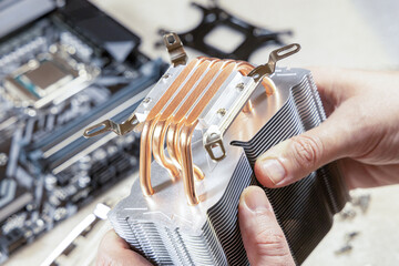 PC assembly. Technician's hands hold new CPU heatsink. Close-up