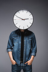 Wall Mural - Young man with clock on head and hands in pockets of jeans on grey background, concept of time management