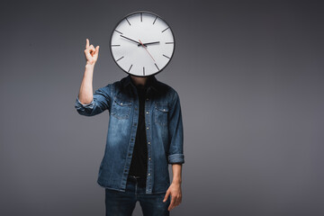 man with clock near face pointing with fingers on grey background, concept of time management