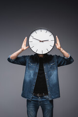Wall Mural - Young man in jeans jacket with clock on head on grey background, concept of time management