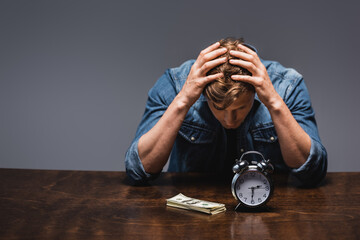 Wall Mural - Dissatisfied man looking at money and alarm clock on table isolated on grey, concept of time management