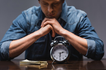 Wall Mural - Selective focus of money and alarm clock on table near pensive man isolated on grey, concept of time management