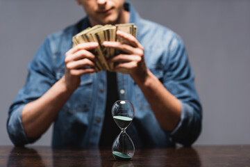 Wall Mural - Selective focus of hourglass on table and man holding money isolated on grey, concept of time management