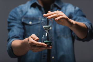 Wall Mural - Cropped view of man holding hourglass with flowing sand isolated on grey, concept of time management