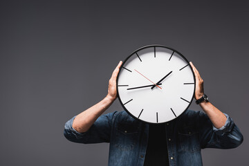 Wall Mural - Young man holding wall clock near head on grey background, concept of time management