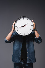 Wall Mural - Young man holding clock near face on grey background, concept of time management