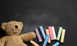 © nndanko - brown teddy bear and colorful crayons on black chalk board