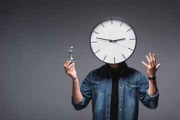 Wall Mural - Man with clock on head holding hourglass and gesturing on grey background, concept of time management