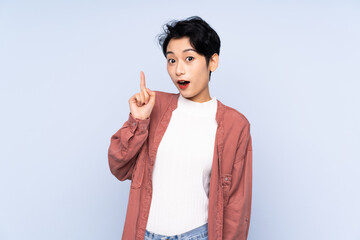 Young Asian girl over isolated blue background thinking an idea pointing the finger up