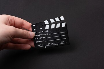 Sticker - Closeup of a person's hand holding a miniature clapperboard against a black background