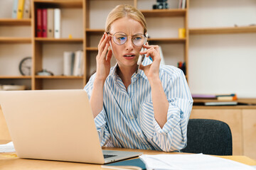 Canvas Print - Image of woman with headache talking on cellphone while using laptop