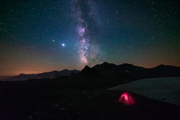 Wall Mural - milky way galaxy stars in the night sky over the alps, illuminated camping tent in foreground, snowc