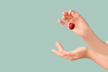 Female hands with sweet cherry on color background