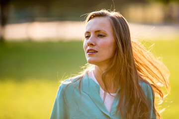Wall Mural - portrait of a young woman with long hair, natural woman outdoor portrait over green grass park background