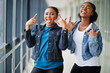 © AS Photo Family - Two african woman friends in jeans jacket show rock fingers  indoor together.