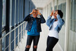 © AS Photo Family - Two african woman friends in jeans jacket showing eyeglasses by fingers indoor together.