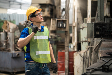 The technician in the factory is maintaining the machine. The technician or engineer is carrying a wrench to fix the machine.