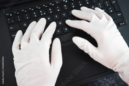 hands typing on shared computer keyboard at work wearing disposable gloves to avoid contact with potentially infected surfaces