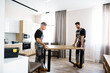 © Svitlana - We make moving easy. Full length shot of two contractor employees, young and aged repairmen in uniform moving personal belongings, table in the kitchen. Service concept