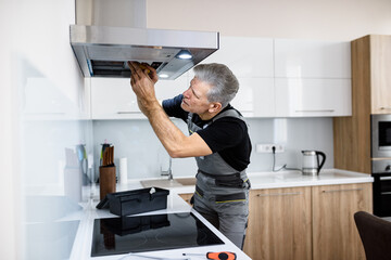 Fixing your technology problem. Aged repairman in uniform working, fixing broken kitchen extractor fan using screwdriver. Repair service concept