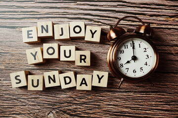 Wall Mural - enjoy your sunday alphabet letter with alarm clock on wooden background