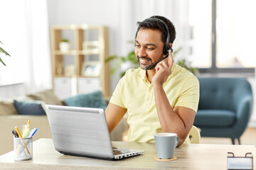 Wall Mural - remote job, technology and people concept - happy smiling indian man with headset and laptop computer having conference call at home office