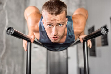 Poster - fitness, sport, bodybuilding and people concept - young man doing push-ups on parallel bars in gym