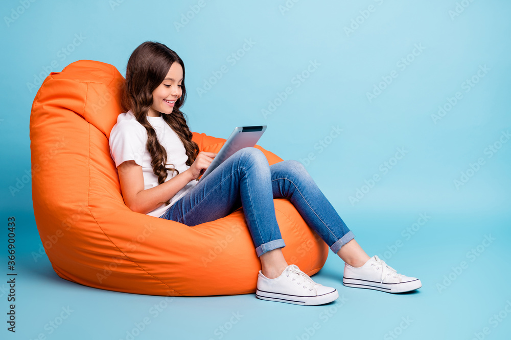 Portrait of nice attractive cheerful cheery focused wavy-haired girl sitting in chair using tablet ebook isolated on bright vivid shine vibrant blue teal turquoise color background - obrazy, fototapety, plakaty 