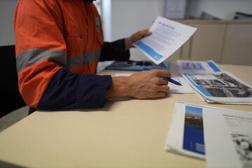 Safety workplace construction worker setting on a chair holding a pen while reading site safety induction rule and regulation evacuation plan prior first time working on site