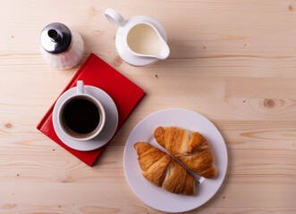 a white ceramic cup with black espresso, french croissant as breakfast or snack concept on rustic, natural texture wooden surface