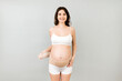 © sosiukin - Portrait of pregnant woman in underwear dressing orthopedic bandage to reduce pain in the back at gray background with copy space. Orthopedic abdominal support belt concept