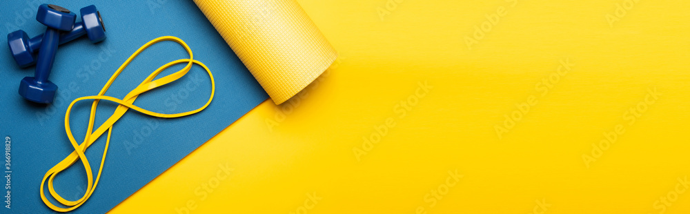 top view of blue fitness mat with dumbbells and resistance band on yellow background, panoramic shot - obrazy, fototapety, plakaty 