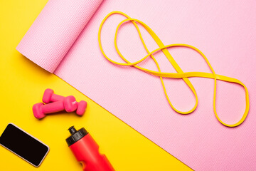 Poster - top view of resistance band on pink fitness mat near smartphone, sports bottle, dumbbells on yellow background